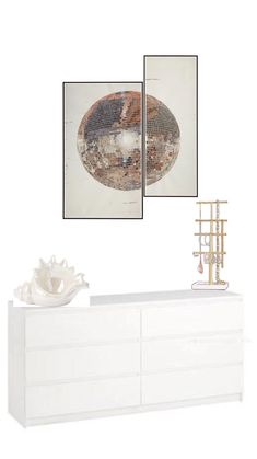 a white dresser with two pictures on the wall above it and a sculpture in front of it