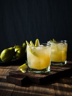 two glasses filled with lemonade sitting on top of a wooden cutting board next to limes