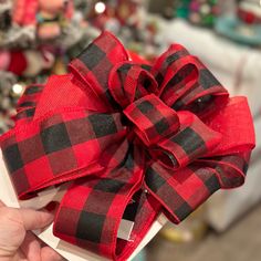 a hand holding a red and black bow on top of a white box with christmas decorations in the background