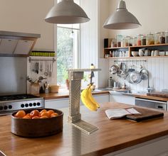 a kitchen with two hanging lights over the island and a bowl of fruit on the counter