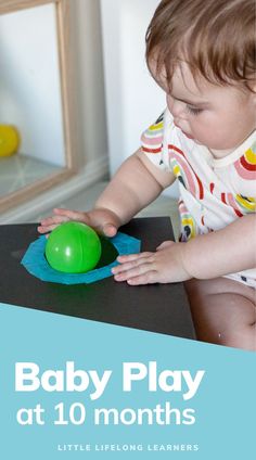 a baby playing with a green ball on top of a table