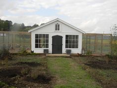 a small white house sitting in the middle of a field next to a fenced off area