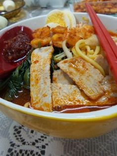 a bowl filled with noodles, meat and vegetables next to chopsticks on a table