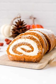 a cinnamon roll with cream cheese frosting on a cutting board next to pumpkins and pine cones