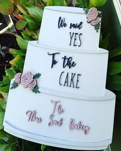 three tiered cake with flowers and words on it's side sitting in front of some plants