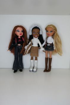 three dolls standing next to each other in front of a white wall and two are wearing boots