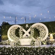 an outdoor wedding setup with white flowers and greenery on the wall, surrounded by string lights