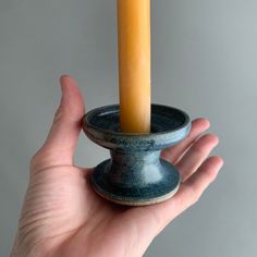 a hand holding a small candle holder with a single pillar in it's center