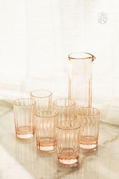 an assortment of glassware sitting on top of a marble countertop next to a vase