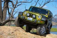 a green jeep parked on top of a dirt hill next to a body of water