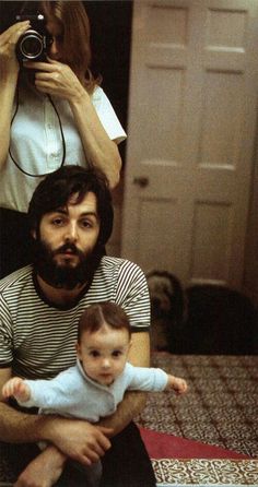 a man sitting on the floor holding a baby and taking a photo with a camera