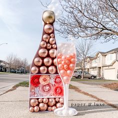 a wine glass and bottle shaped sculpture on the side of a street with houses in the background