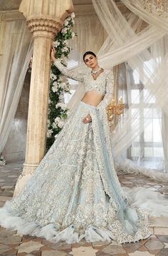 a woman in a white and blue lehenga standing next to a chandelier