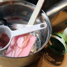 a metal pot filled with food next to a wooden spoon and utensils on top of a table