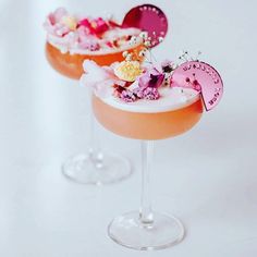 two glasses filled with drinks sitting on top of a white table next to each other