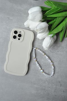 a white phone case sitting on top of a table next to flowers and a beaded bracelet