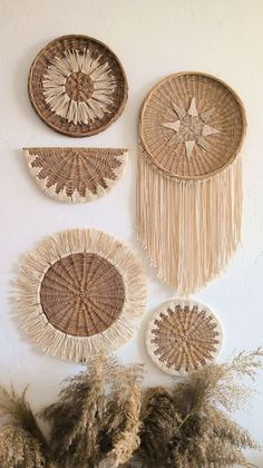 three woven baskets hanging on the wall with plants in front of them and dried grass