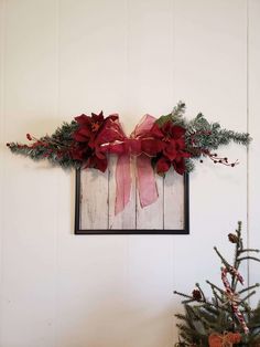 a christmas wreath with poinsettis and greenery hangs on the wall next to a small tree