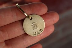 a hand holding a gold colored personalized keychain with a house on it