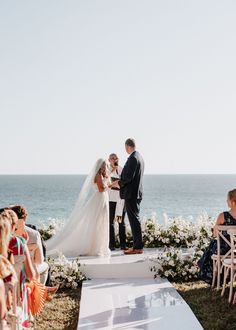 a bride and groom standing at the end of their wedding ceremony by the ocean in front of them