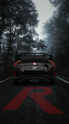 the rear end of a black sports car on a road with trees in the background