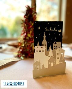 a card with a christmas scene on it sitting on a table next to a tree