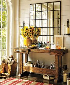 a wooden table with sunflowers and bottles on it in front of a window