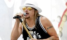 a man with long hair wearing sunglasses and a hat singing into a microphone on stage