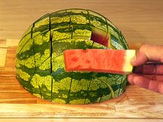 a person cutting up a piece of watermelon on top of a wooden board