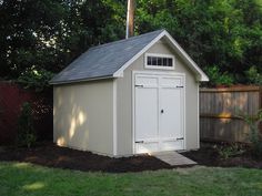 a white shed sitting in the middle of a yard next to a fence and trees