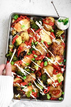 a person is holding a spoon over a tray of food that includes potatoes, broccoli and peppers