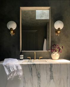 a bathroom with marble counter top and two lights on the wall, along with a large mirror