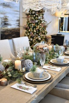 a dining room table set with place settings and christmas decorations on it, along with a lit tree in the background