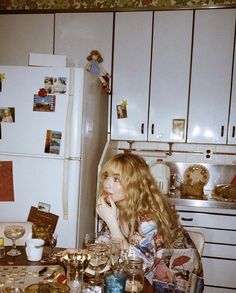 a woman sitting at a kitchen table filled with wine glasses and other things in front of her