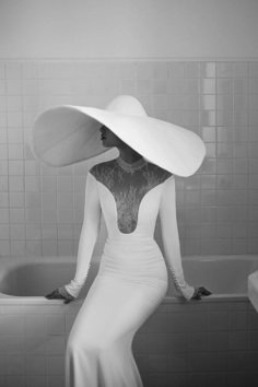 a woman in a white dress and hat sitting on a bathtub with her hands on her hips