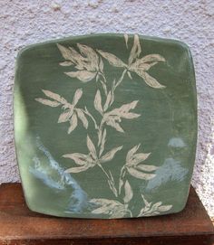 a green plate with white leaves on it sitting on top of a wooden stand next to a wall