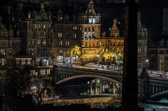 a train traveling over a bridge in the middle of a city at night with lights on