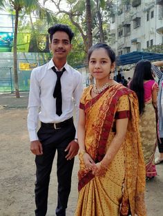 a man standing next to a woman in a yellow sari on a dirt ground