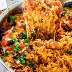 a large pot full of mexican rice and vegetables being lifted with a spatula from it