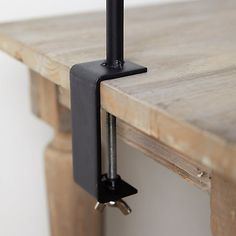 a wooden table with a black metal object on it's end and a white wall in the background