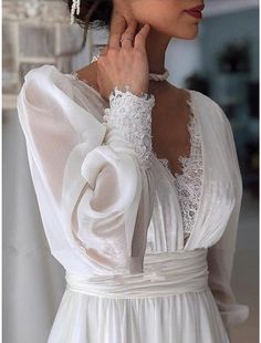 a woman is wearing a white dress with lace on the neck and sleeves, while holding her hand near her face