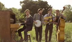 three men are standing in the grass with their instruments and one man is playing an instrument