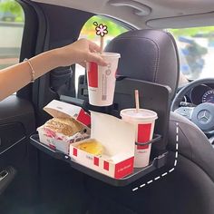 a woman is holding a tray with food and drinks in the back seat of a car