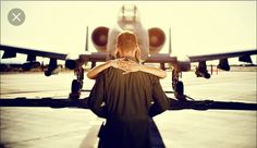 a man and woman standing in front of an airplane on the tarmac with their arms around each other