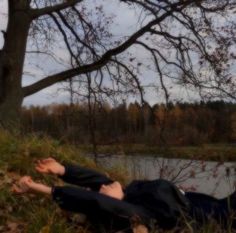 a man laying on the ground next to a tree and water with his eyes closed