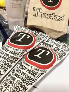 there is a paper bag with the letter t on it next to some cups and napkins