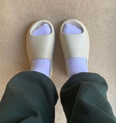 someone wearing green pants and white shoes with purple socks on their feet while standing in front of a carpeted floor