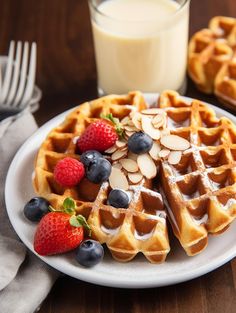 a plate with waffles, berries and almonds next to a glass of milk