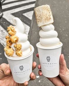 two people holding up ice cream cones with toppings in their hands on the street