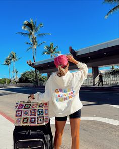 a woman in shorts and a white sweatshirt is pulling a black suitcase down the street